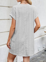 Woman wearing a gray patterned dress standing against a light-colored wall.