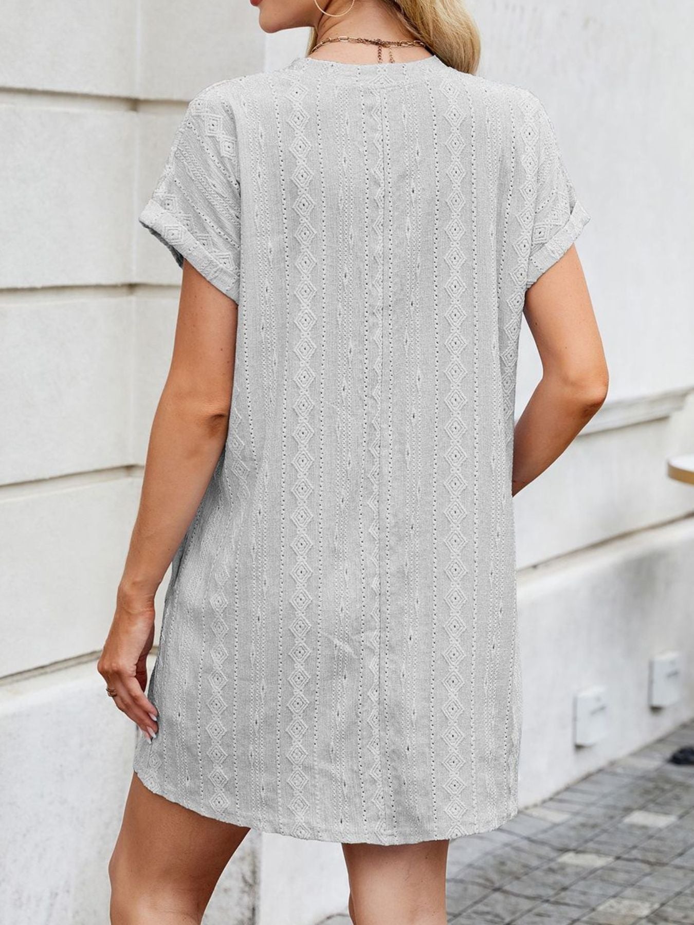 Woman wearing a gray patterned dress standing against a light-colored wall.