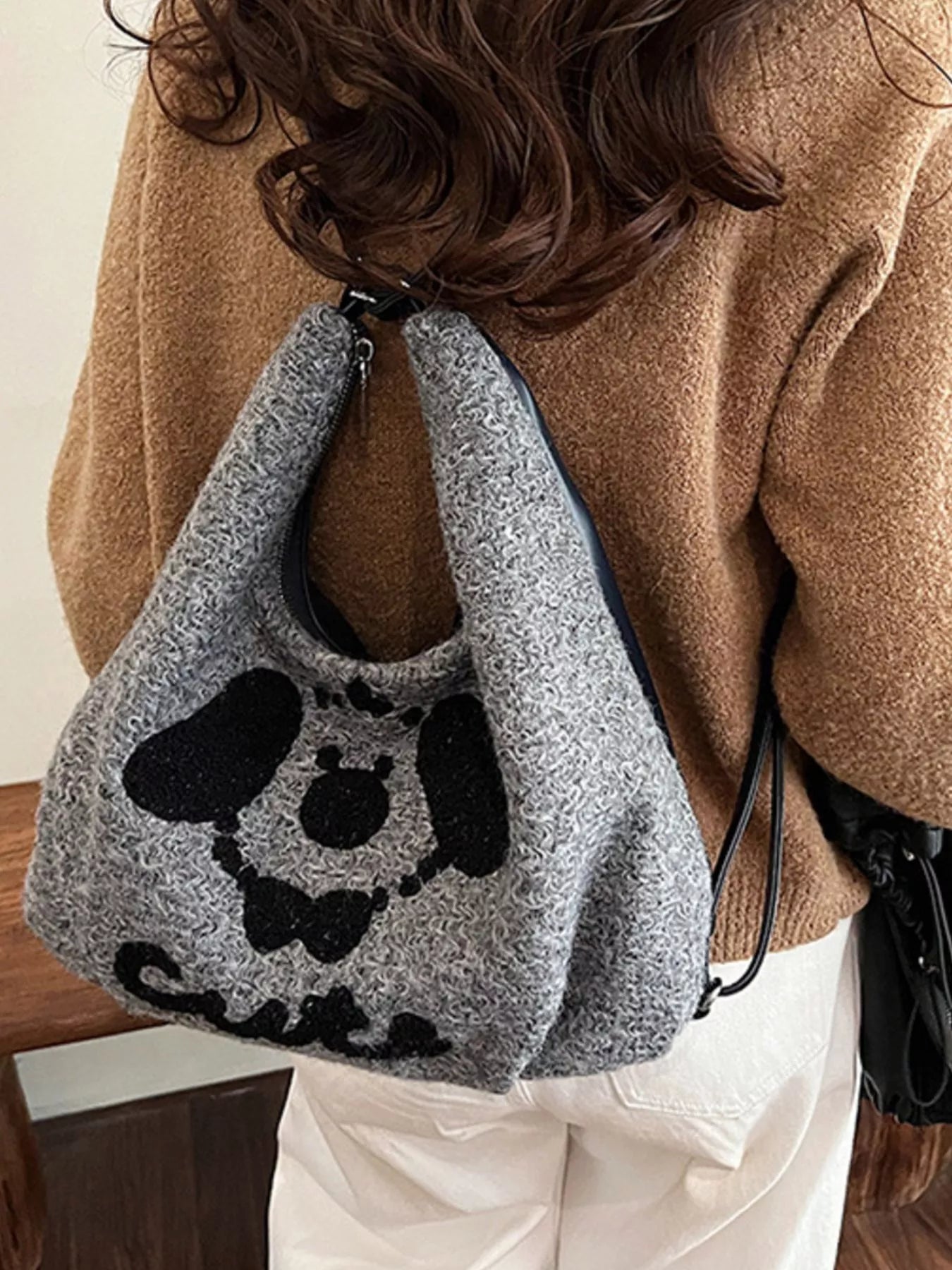 Person wearing a gray knitted bag with a black dog design, standing indoors.