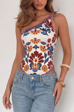 Woman wearing a colorful floral one-shoulder top and blue jeans against a white background