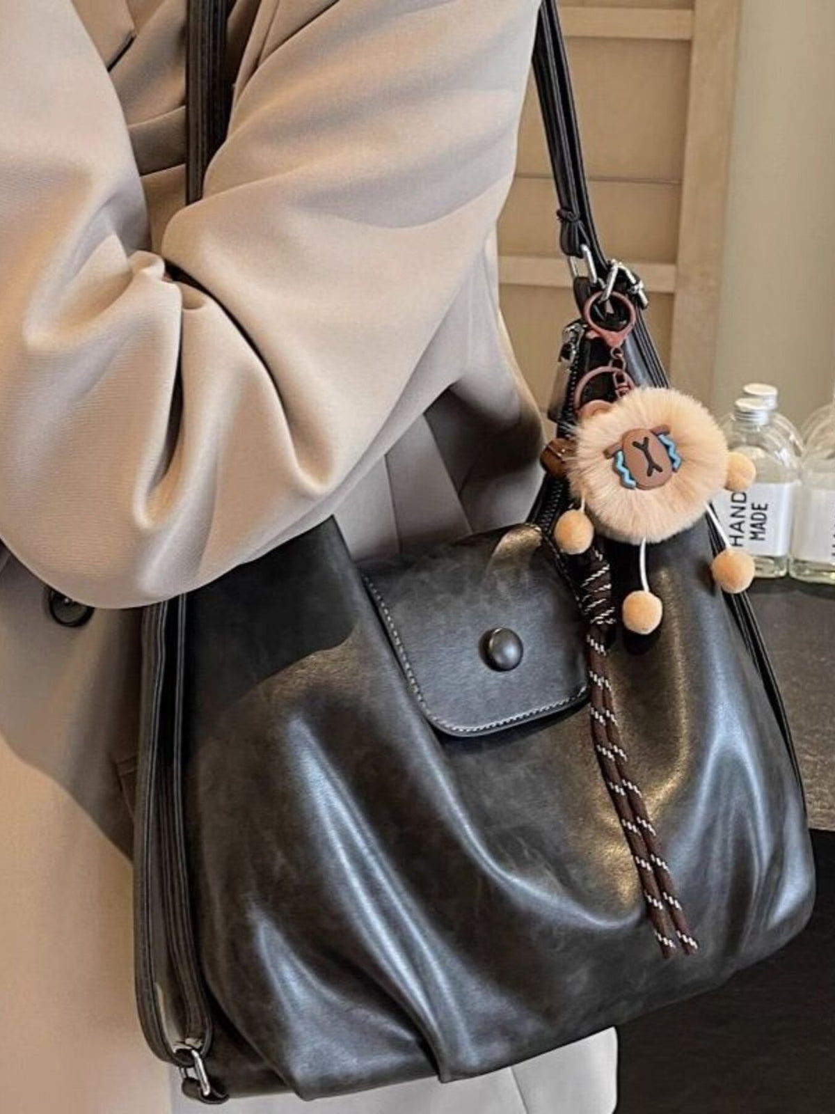 Black handbag with decorative keychain held by a person wearing a beige coat.