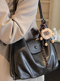 Black handbag with decorative keychain held by a person wearing a beige coat.