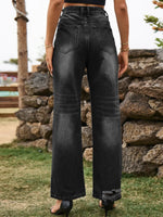 Person wearing black wide-leg jeans standing in front of a stone wall.