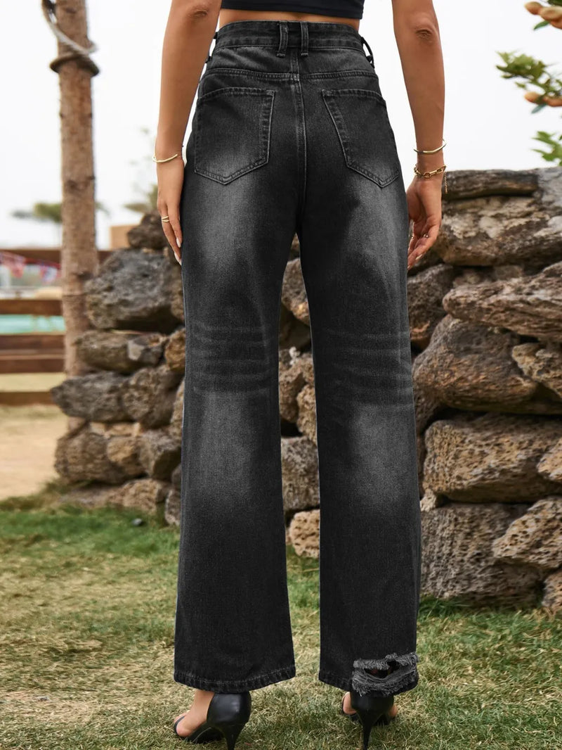 Person wearing black wide-leg jeans standing in front of a stone wall.