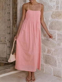 Woman wearing a pink dress standing against a stone wall.