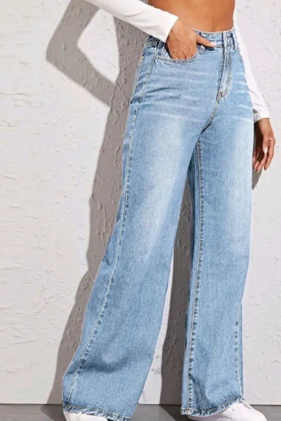Person wearing light blue wide-leg jeans against a white brick wall.