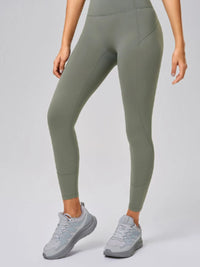Person wearing olive green leggings and gray sneakers on a light gray background