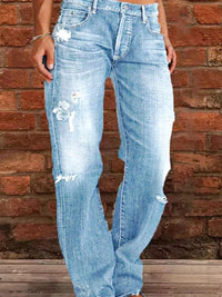 Person wearing light blue distressed jeans against a brick wall.