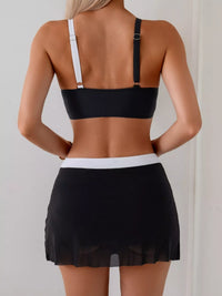 Person wearing a black bikini top and black skirt against a plain background