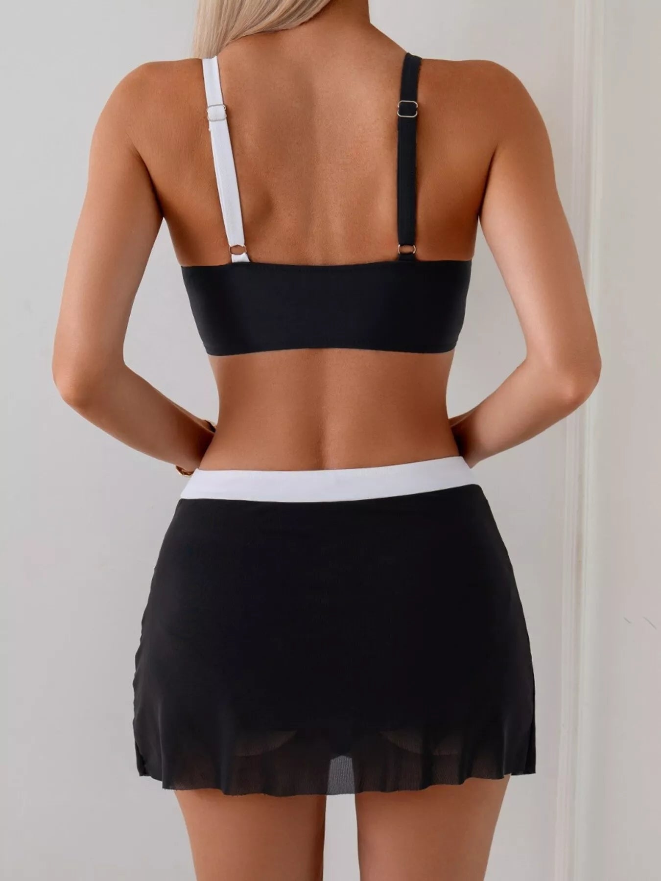Person wearing a black bikini top and black skirt against a plain background