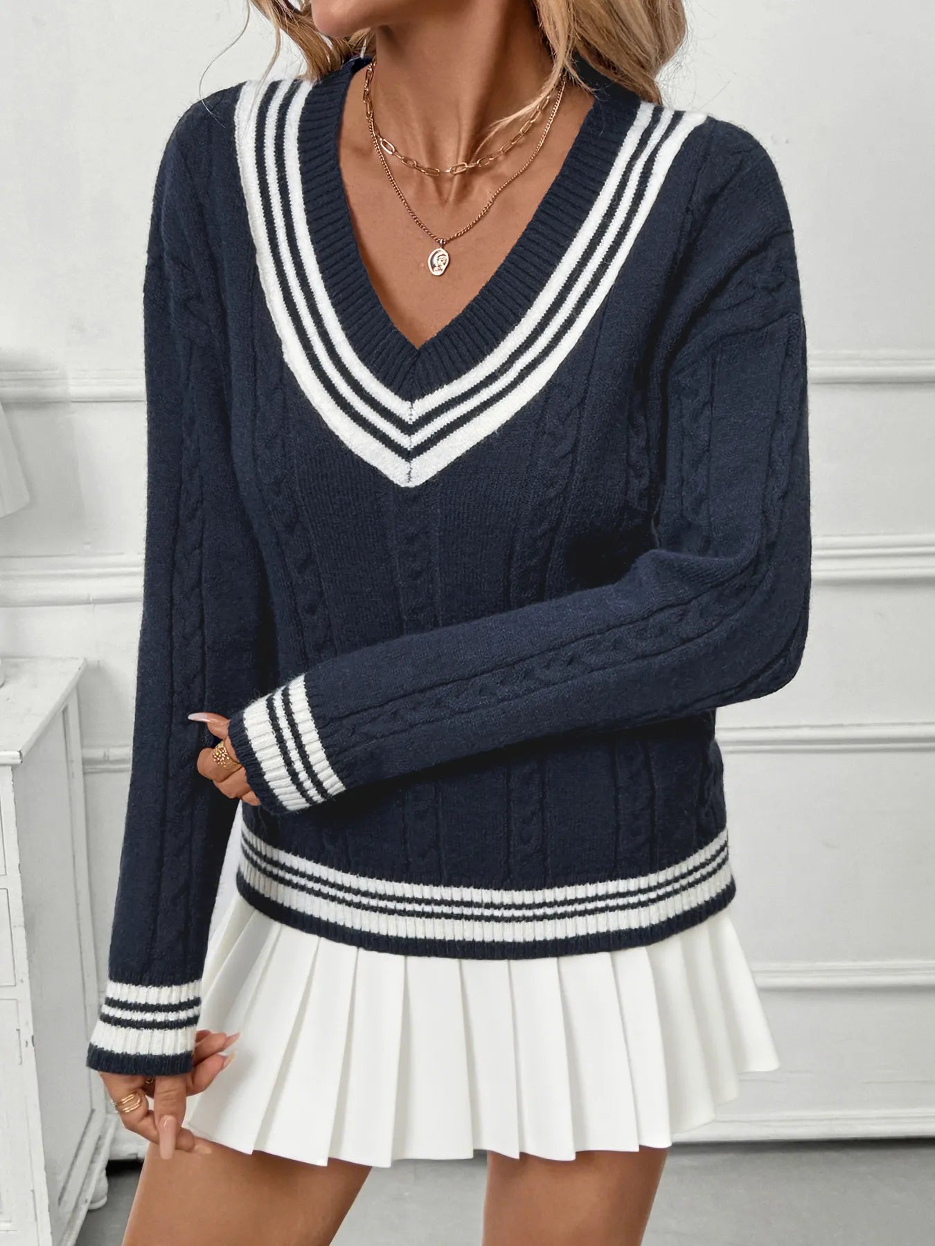 Navy blue sweater with white stripes worn by a person, paired with a white pleated skirt.