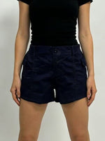 Person wearing navy shorts and a black top on a plain background
