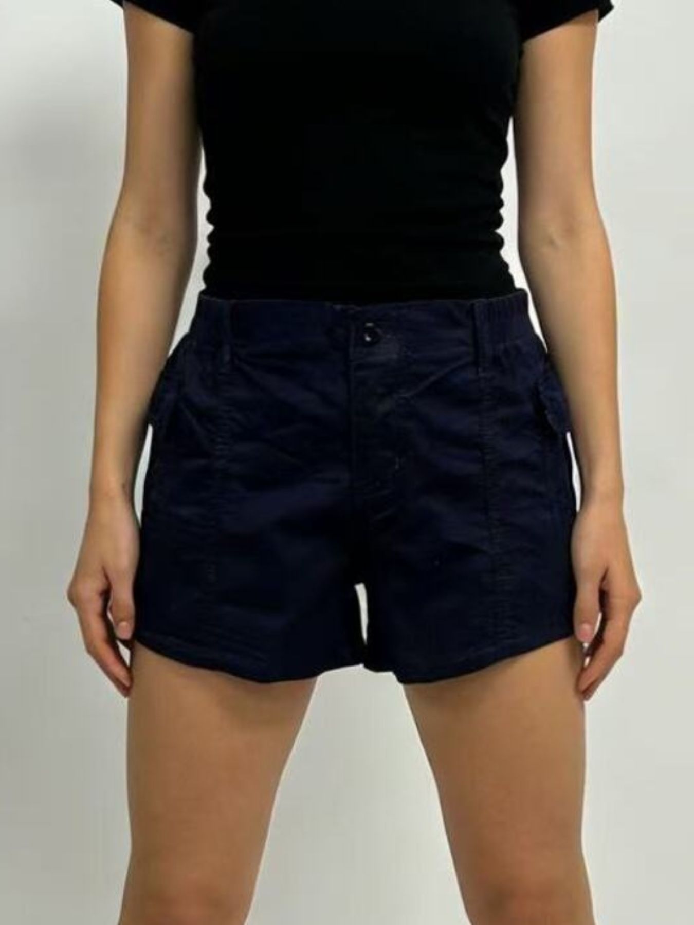 Person wearing navy shorts and a black top on a plain background