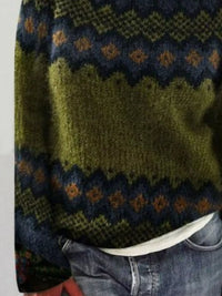 Close-up of a green knitted sweater with a pattern, worn over a white shirt and blue jeans.