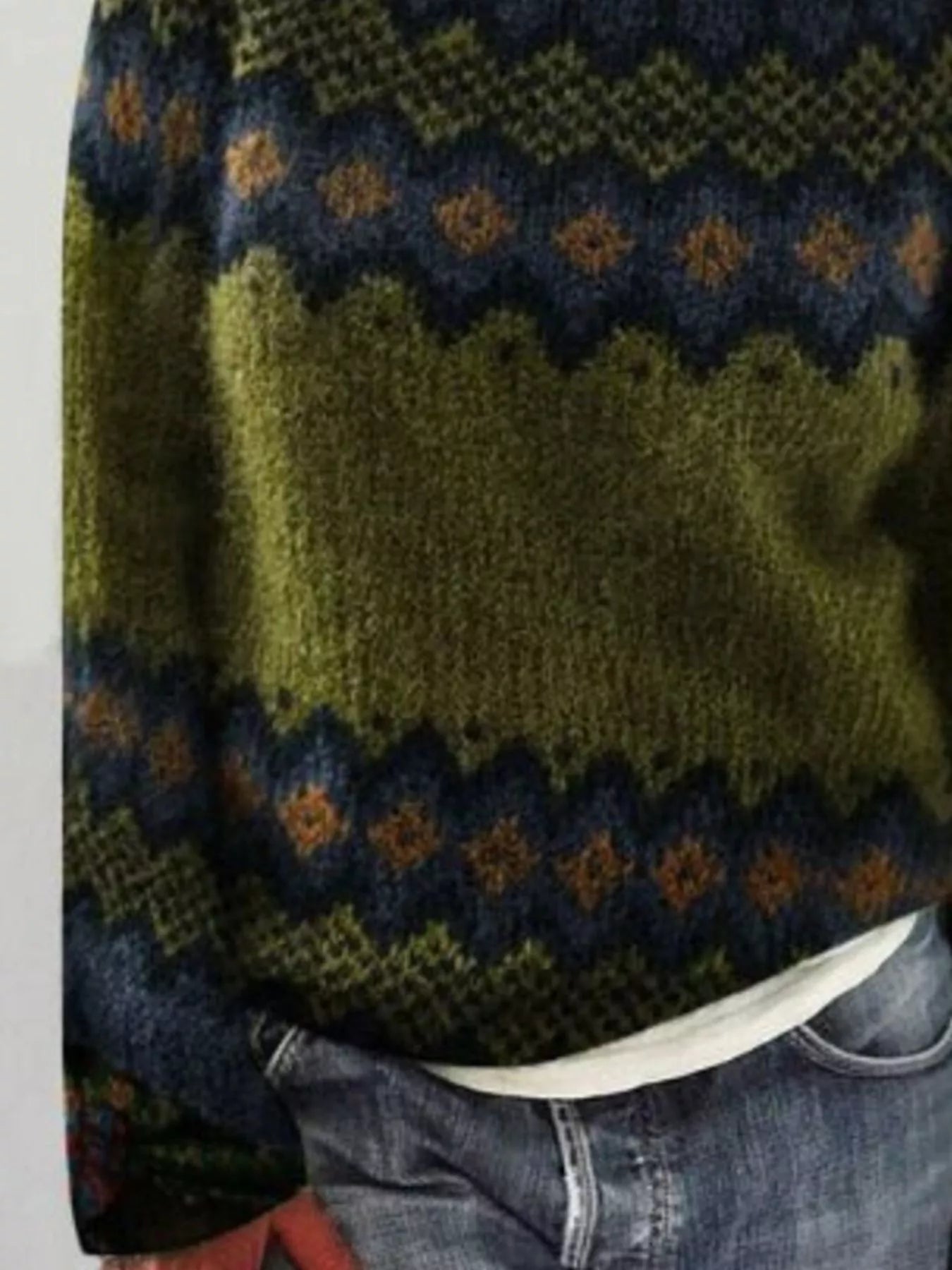Close-up of a green knitted sweater with a pattern, worn over a white shirt and blue jeans.