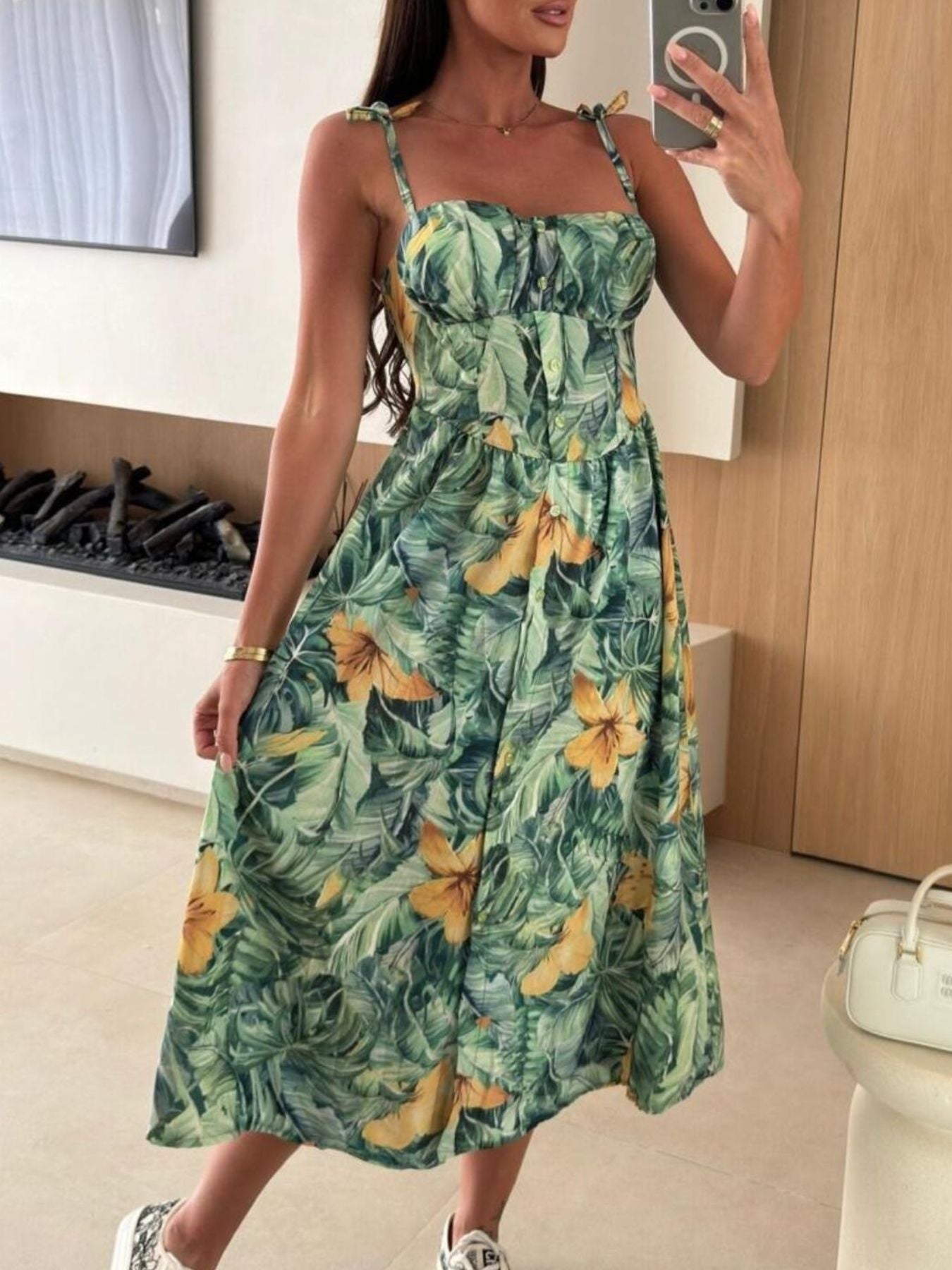 Woman wearing a green floral dress taking a mirror selfie.