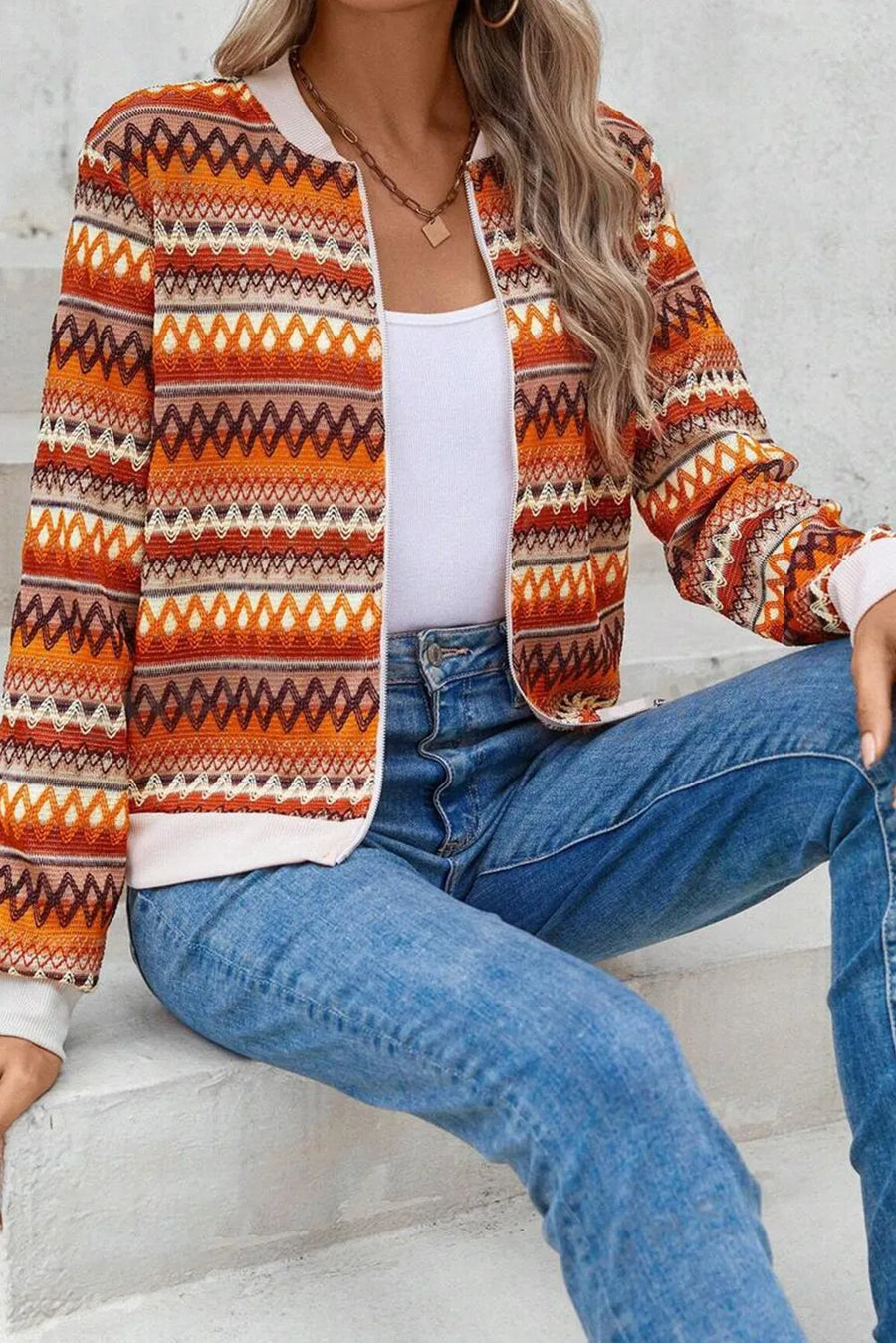 Person wearing a patterned jacket and blue jeans sitting on steps.