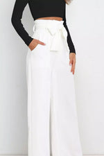 Person wearing a black long-sleeve top and white wide-leg pants with a tie-waist design on a plain background.