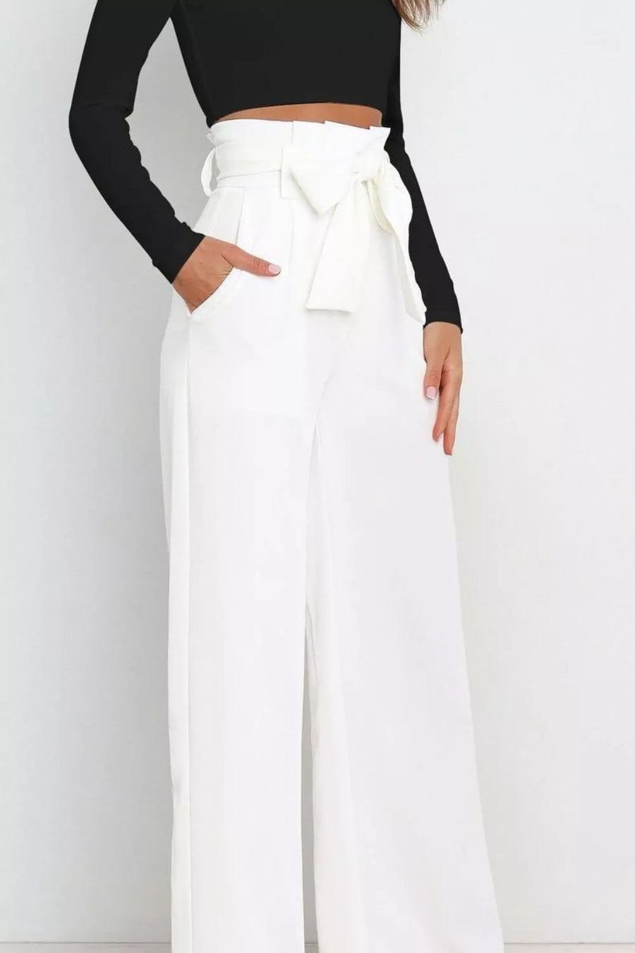 Person wearing a black long-sleeve top and white wide-leg pants with a tie-waist design on a plain background.