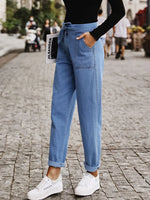 Person wearing blue jeans and white sneakers on a street.
