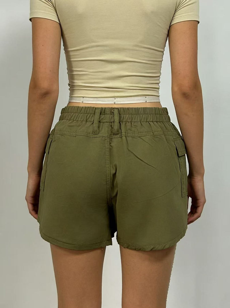 Person wearing olive green shorts and a beige top on a plain background