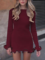 Woman wearing a burgundy dress with long sleeves and scalloped hem in an urban setting.