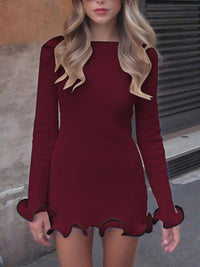 Woman wearing a burgundy dress with long sleeves and scalloped hem in an urban setting.