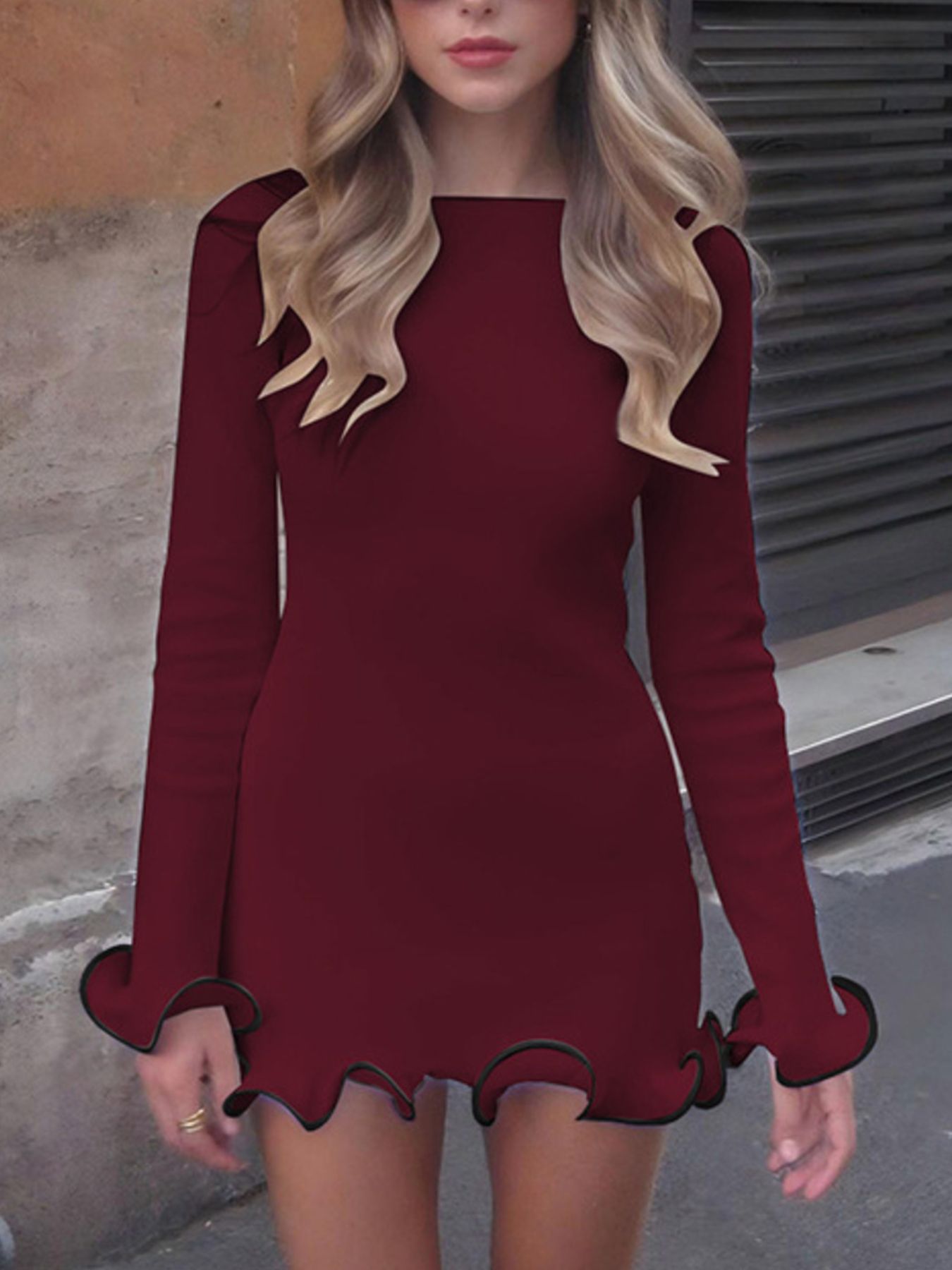 Woman wearing a burgundy dress with long sleeves and scalloped hem in an urban setting.