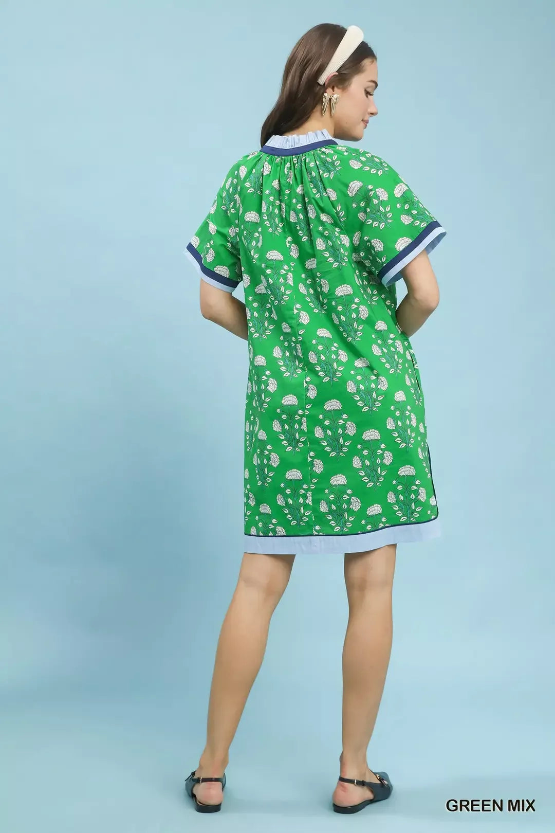 Woman wearing a green dress with white patterns on a light blue background