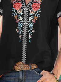 Black blouse with colorful floral embroidery and a leopard print belt.