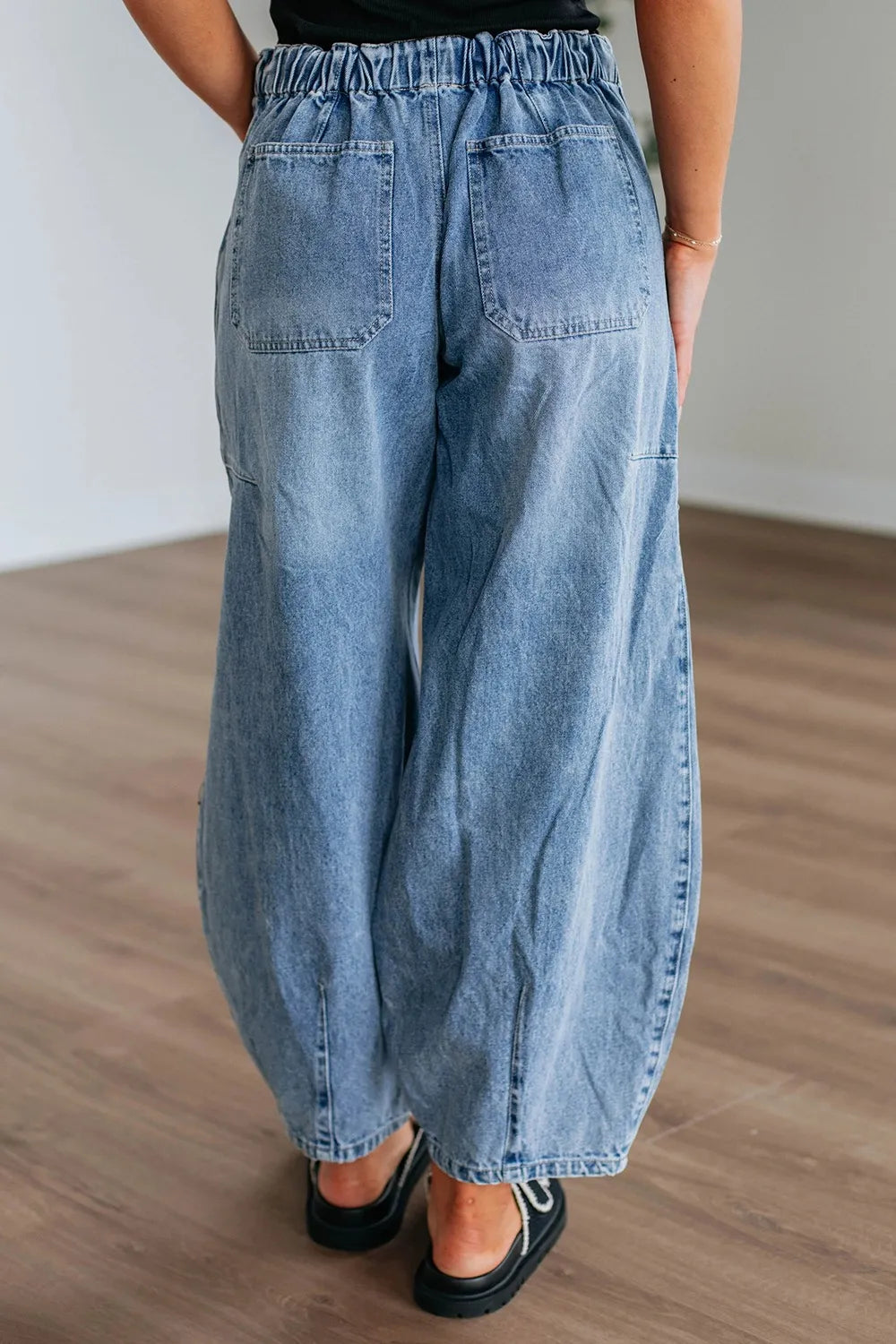 Person wearing wide-leg blue jeans on a wooden floor.