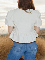 Person wearing a white peplum top and blue jeans standing in a natural setting.