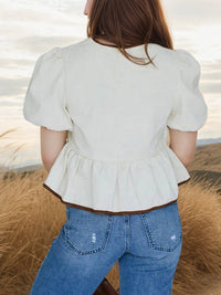 Person wearing a white peplum top and blue jeans standing in a natural setting.