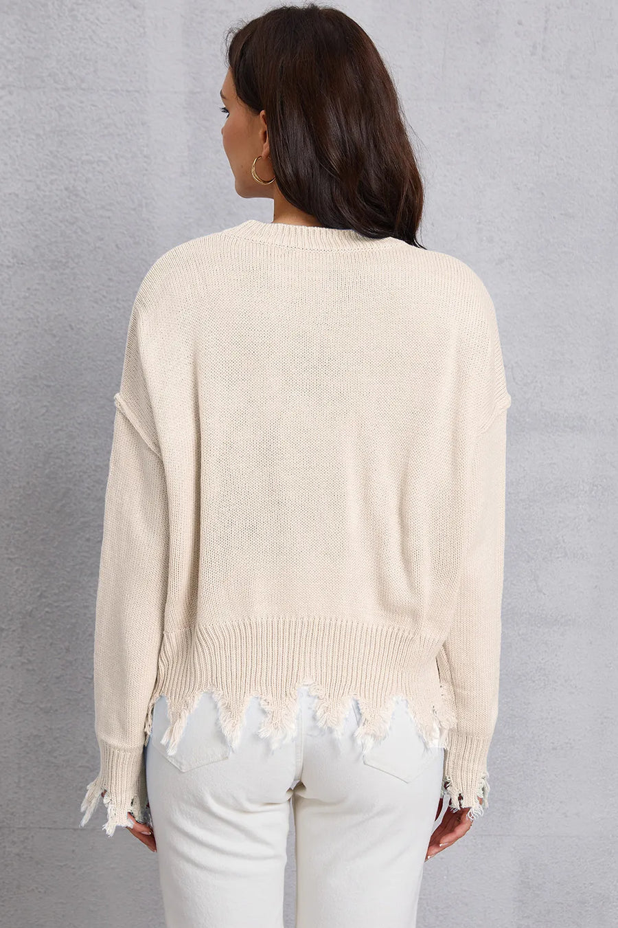 Person wearing a beige sweater with distressed hem and light gray pants against a gray background
