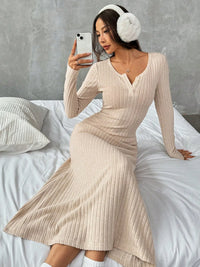 Woman in a beige ribbed dress and white ear muffs taking a selfie on a bed.