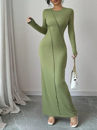 Woman wearing a green long-sleeve dress holding a white handbag indoors.