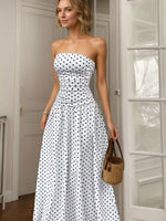 Woman wearing a strapless polka dot dress holding a woven bag indoors.