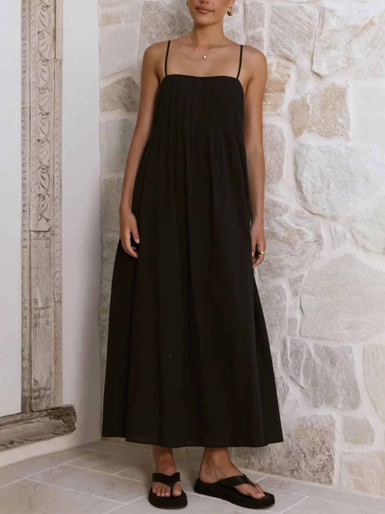 Woman wearing a black slip dress against a stone wall.