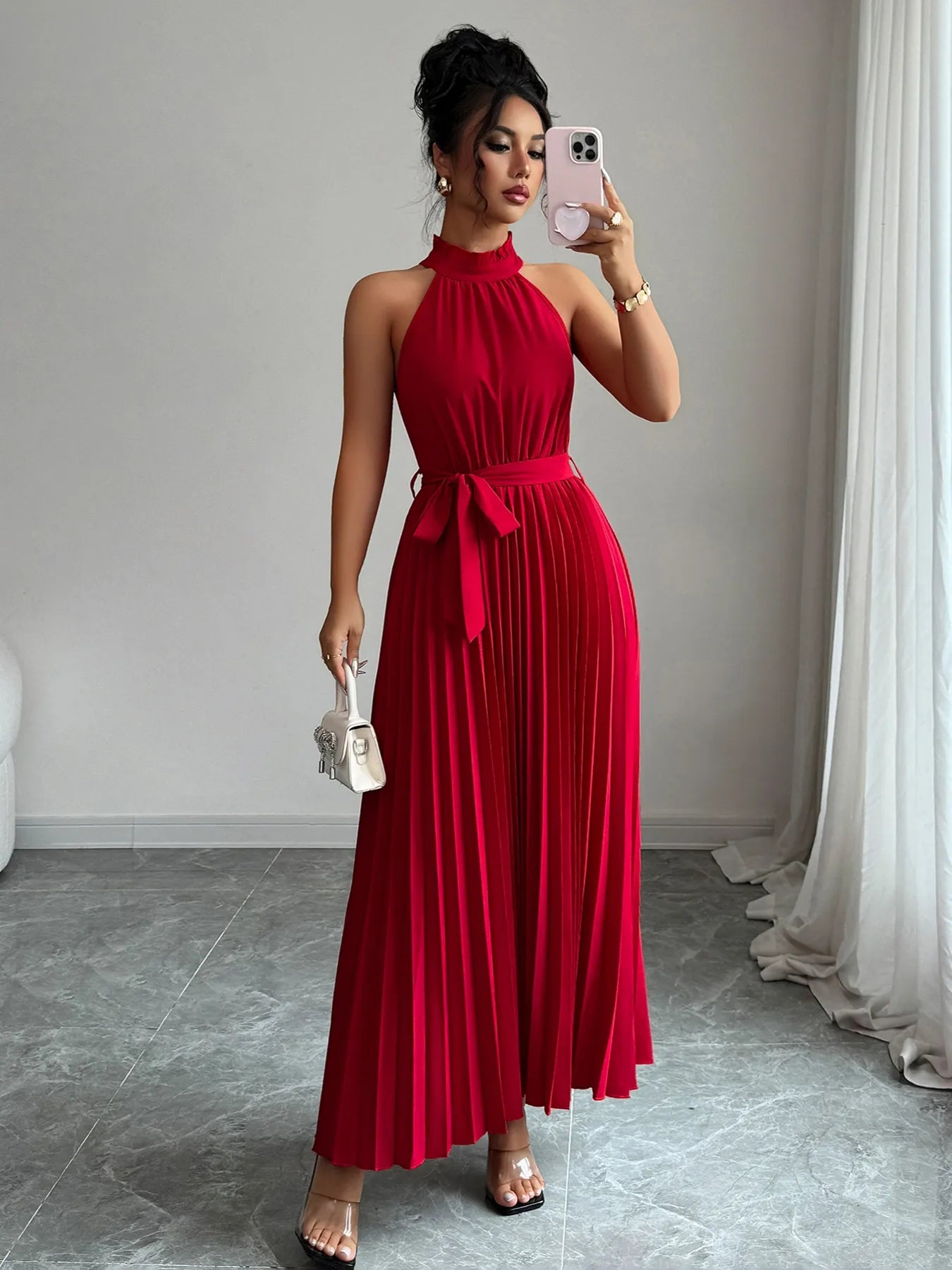 Woman in a red dress taking a mirror selfie in a room with gray walls and white curtains.