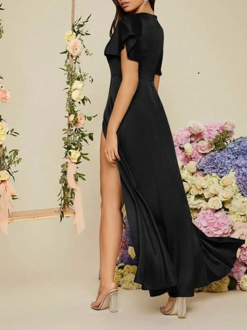 Woman in a black dress with a high slit standing in front of floral decorations.