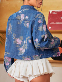 Person wearing a blue floral denim jacket and white skirt indoors.