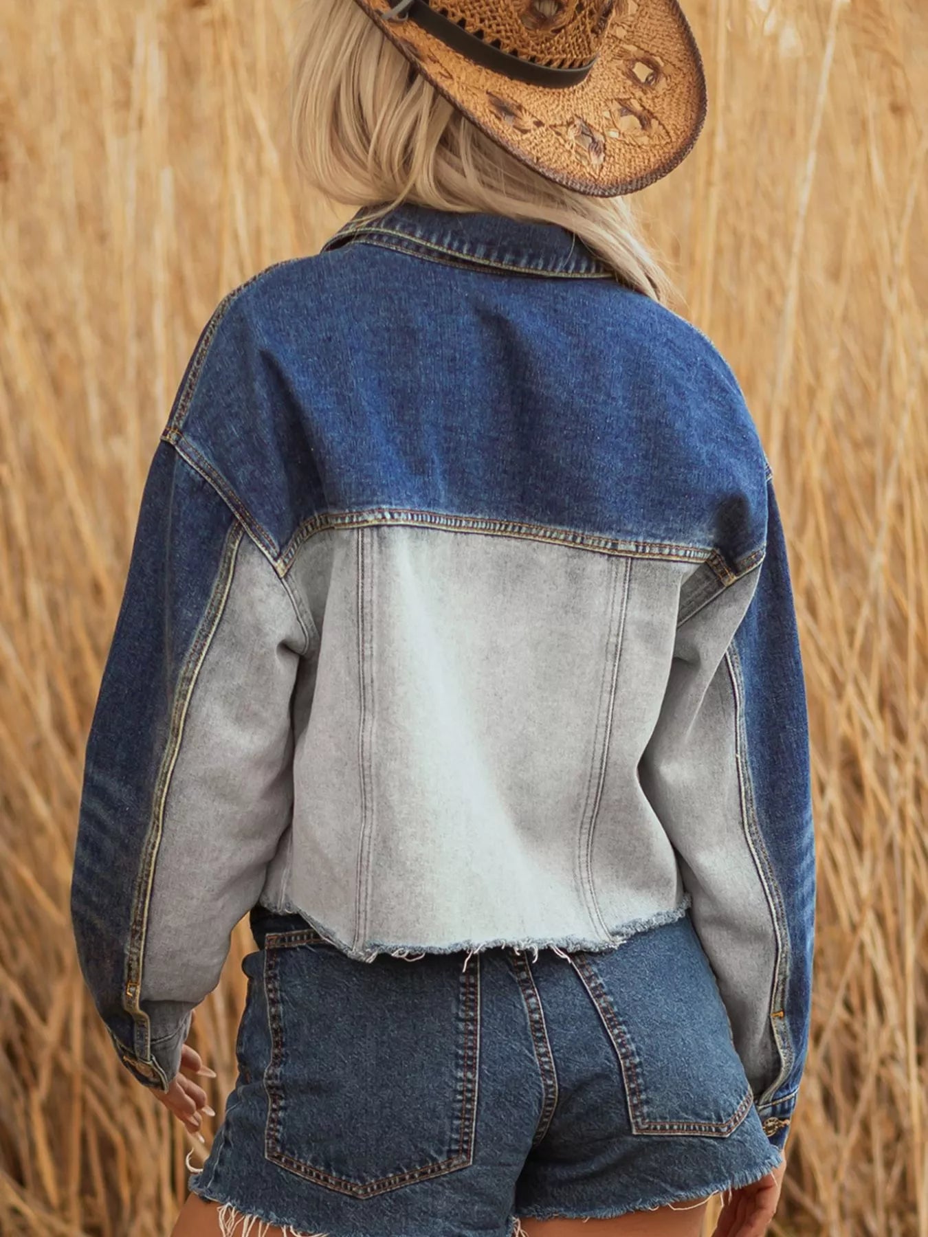 Person wearing a denim jacket and shorts with a straw hat, standing in a field.