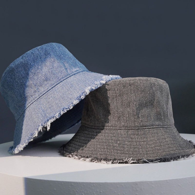 Two bucket hats, one blue and one gray, on a white surface with a dark background.