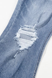 Close-up of a blue denim jeans with a large distressed hole on a white background