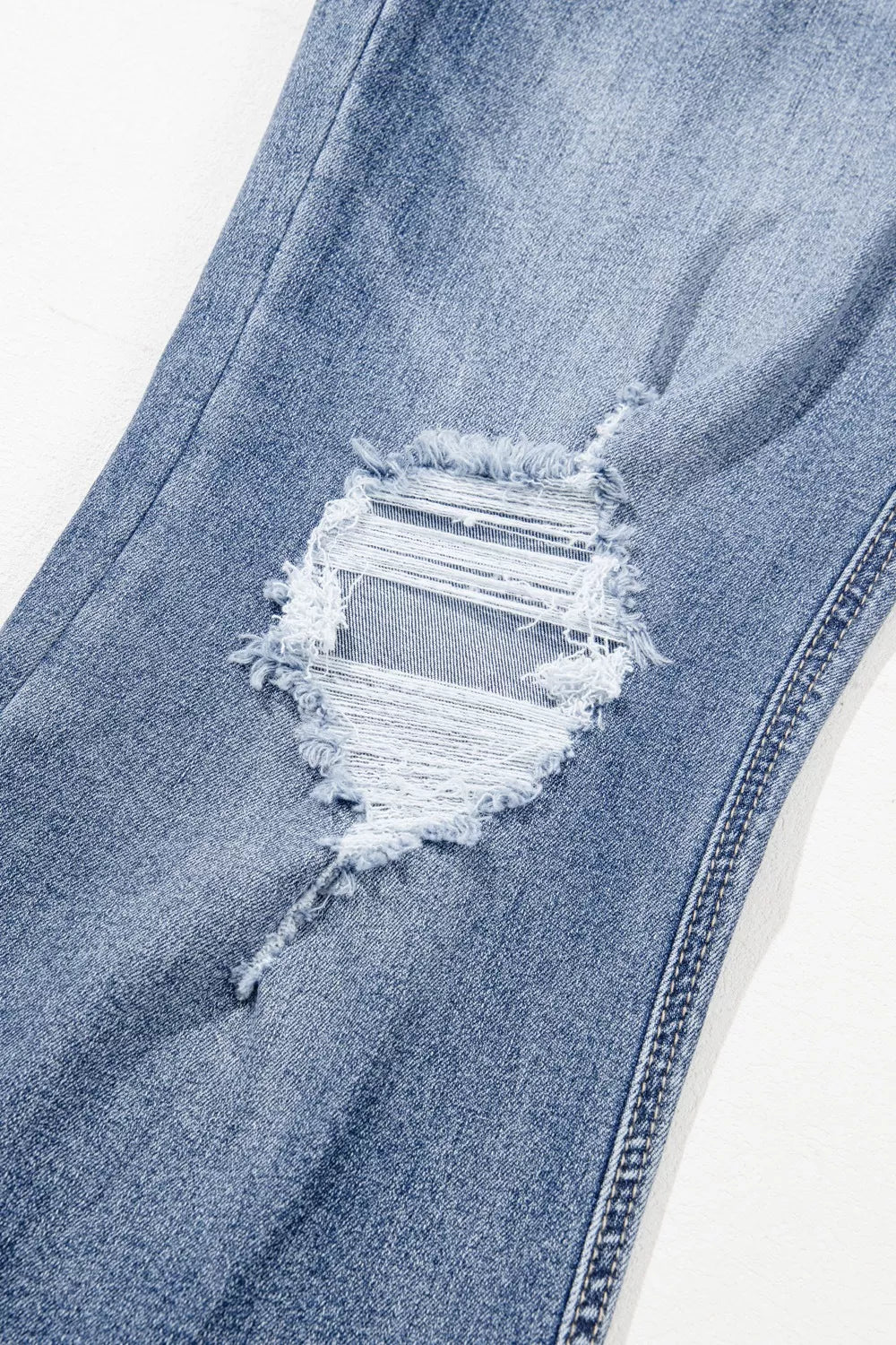 Close-up of a blue denim jeans with a large distressed hole on a white background