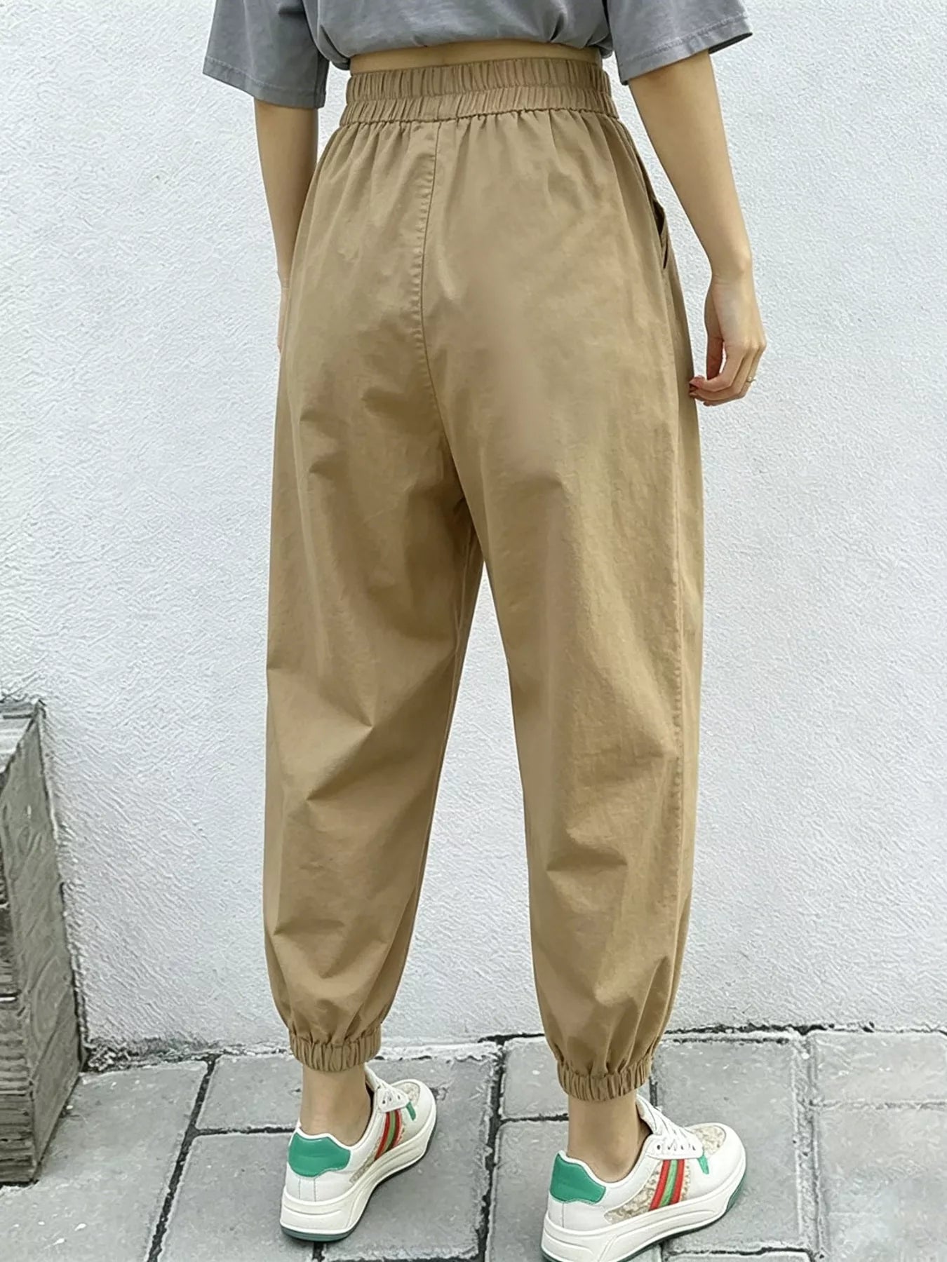 Person wearing beige high-waisted pants with a plain background