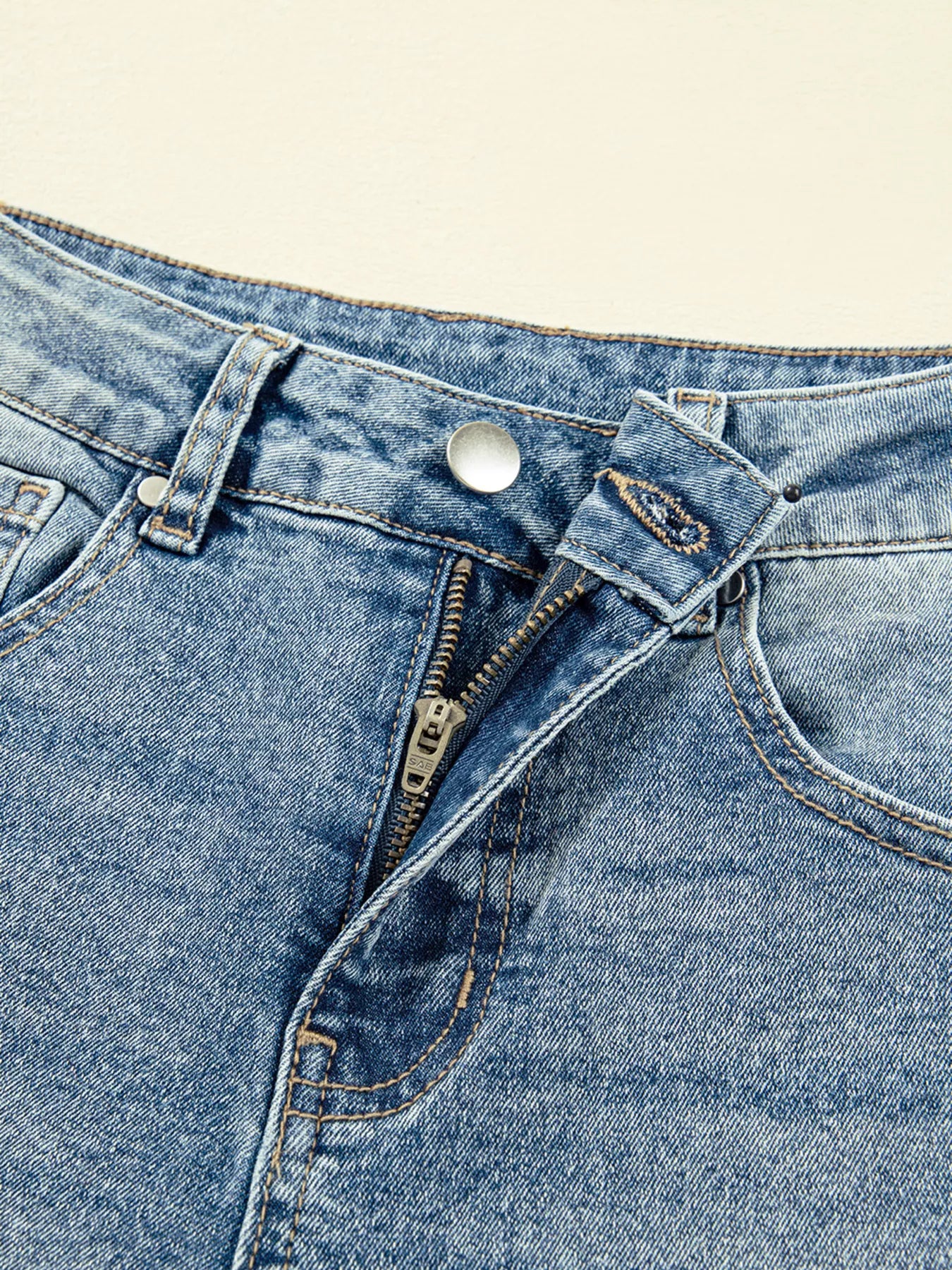 Close-up of a blue denim pocket with zipper and button on a beige background