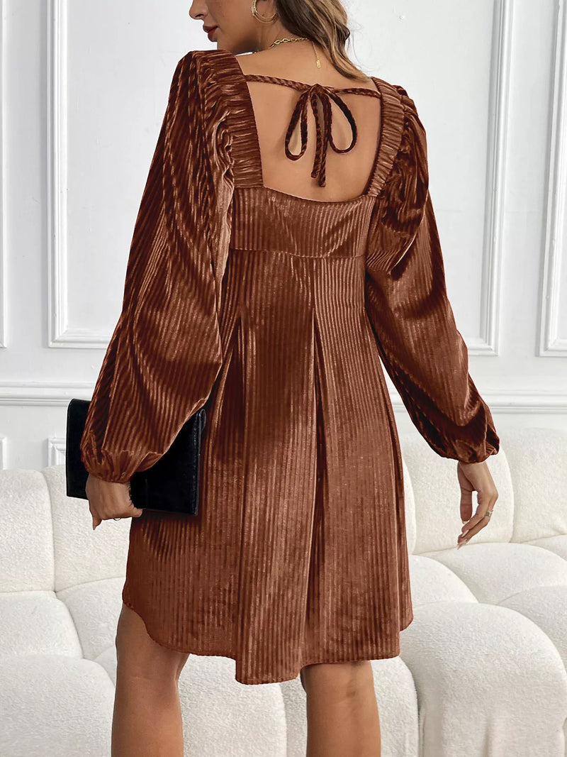 Woman wearing a brown corduroy dress with long sleeves in an indoor setting.