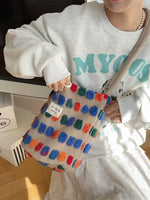 Person wearing a white sweatshirt with teal text, holding a colorful textured bag.