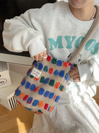 Person wearing a white sweatshirt with teal text, holding a colorful textured bag.